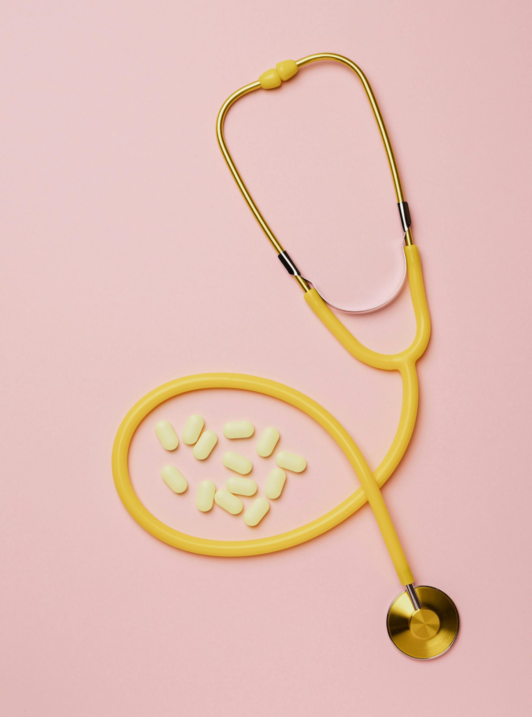 Yellow stethoscope and pills on a pink background, symbolizing healthcare and medicine.