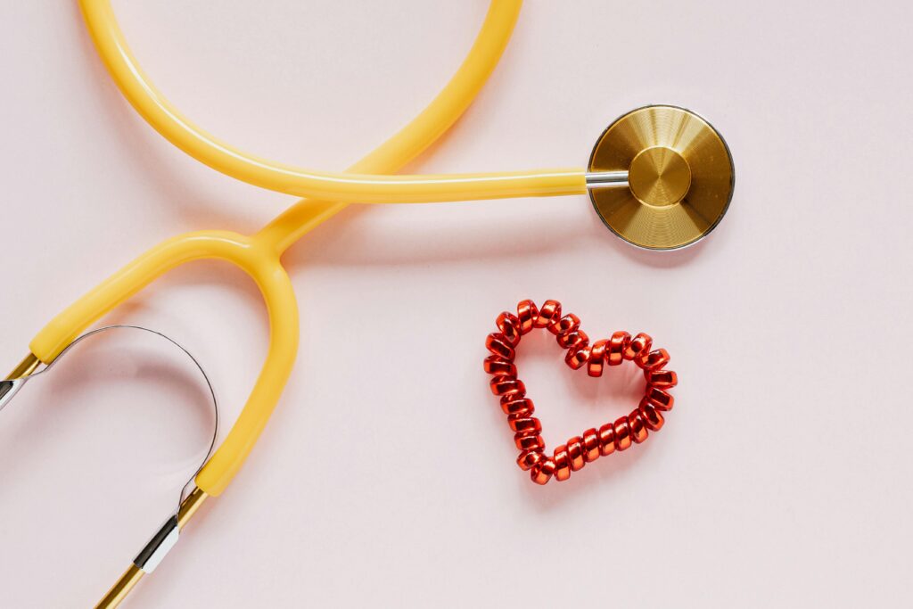 A yellow stethoscope and red heart decoration symbolize love and healthcare on soft pink.