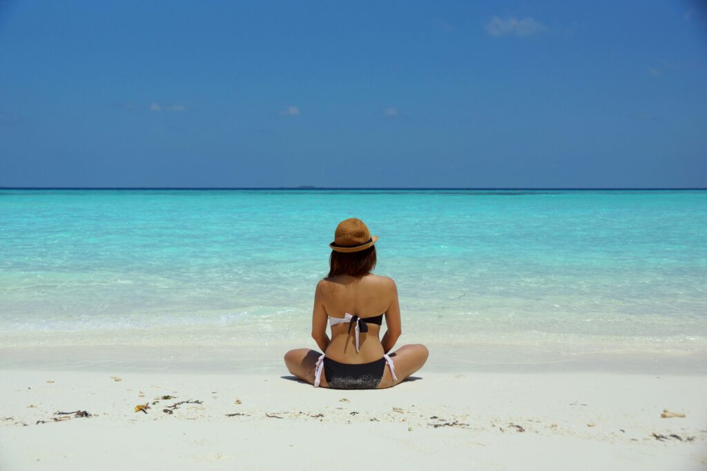 Rear view of a woman in a bikini and hat relaxing on a pristine beach in Maldives.